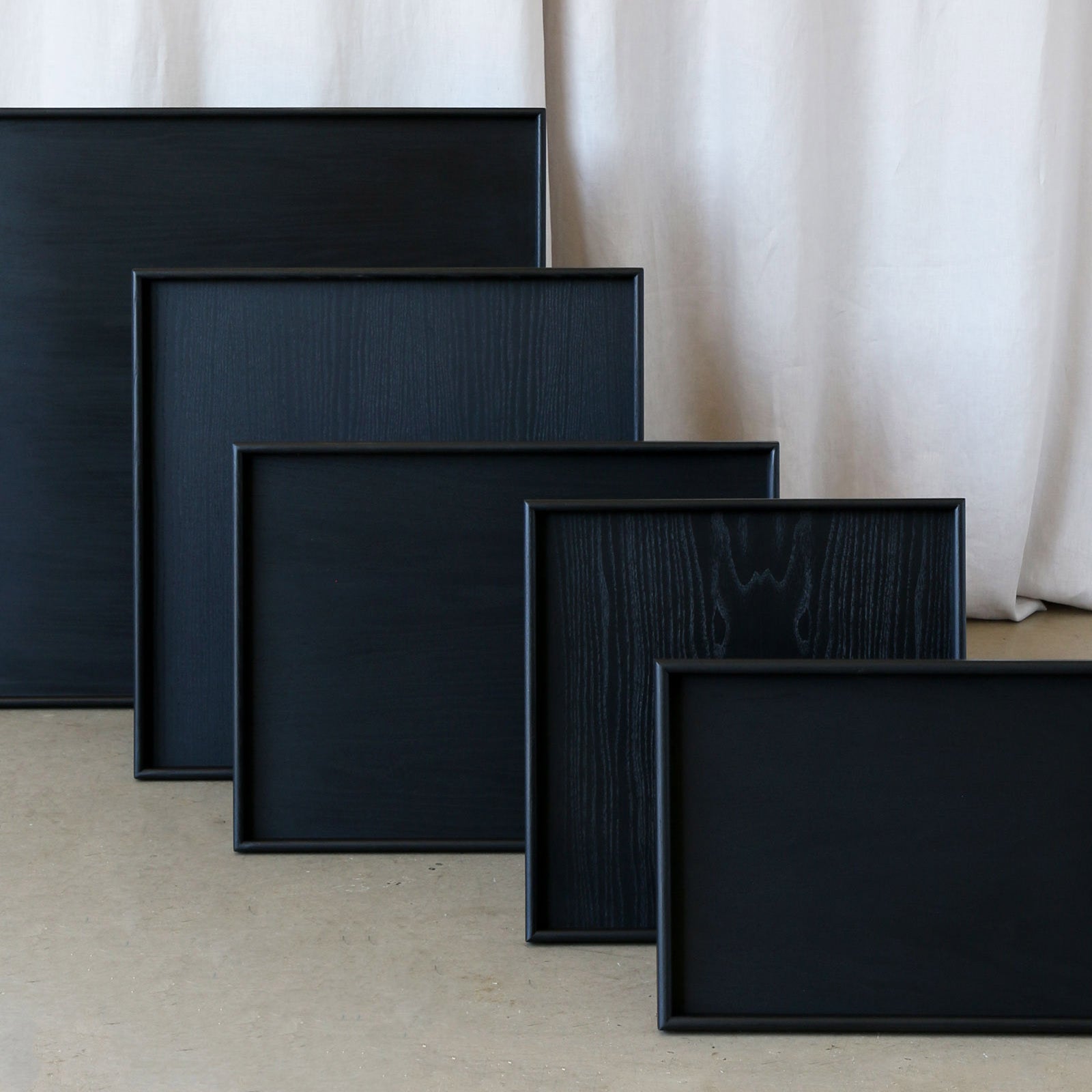 A set of handcrafted trays in black wood, displayed in multiple sizes, ideal as a wooden tray for footstool or coffee table tray.