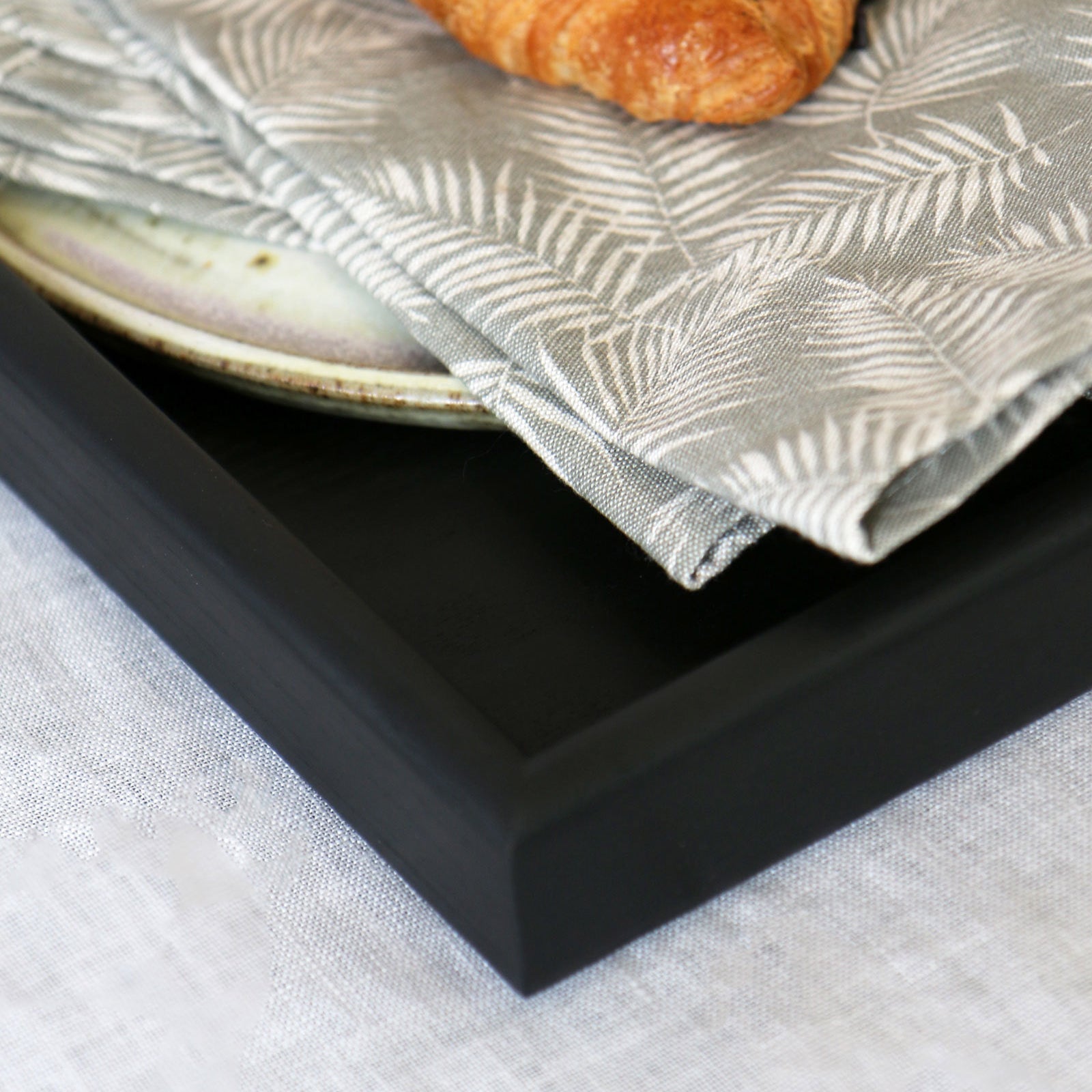 Close-up of a handcrafted tray, highlighting its smooth black finish and sharp edges, making it a stylish wooden tray for footstool or tabletop use.