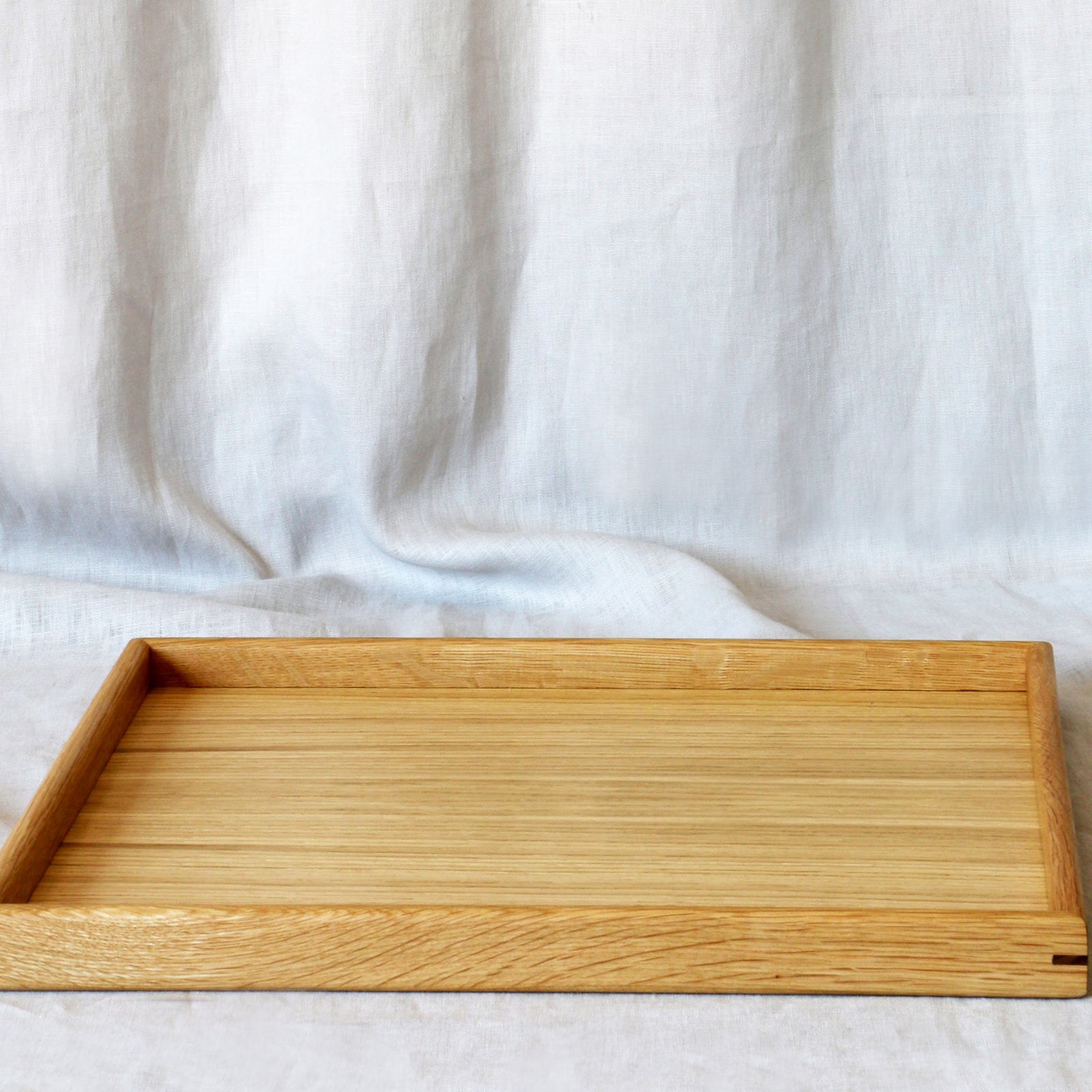 A medium-sized wooden tray for footstool, crafted from oak, displayed on a neutral fabric background.