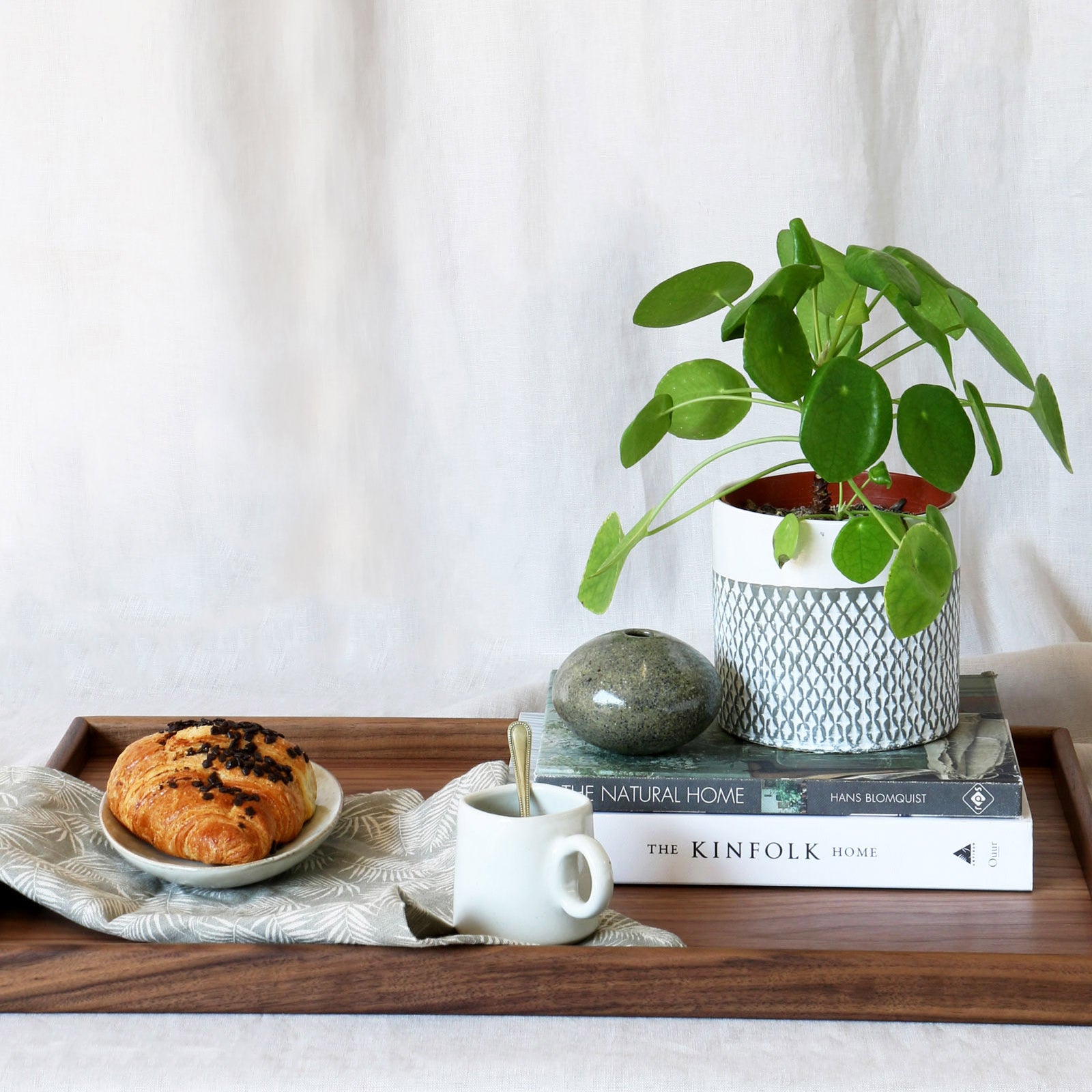 A decorative tray styled with books, a plant, and a pastry, showcasing its elegant functionality in a cozy setting.