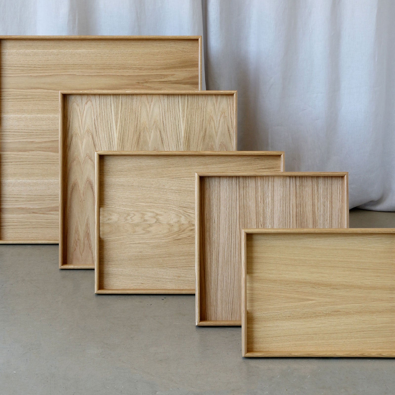 Set of five handcrafted wooden trays displayed in a cascading arrangement, made from light oak wood, ideal as decorative trays or a wooden tray for footstools.