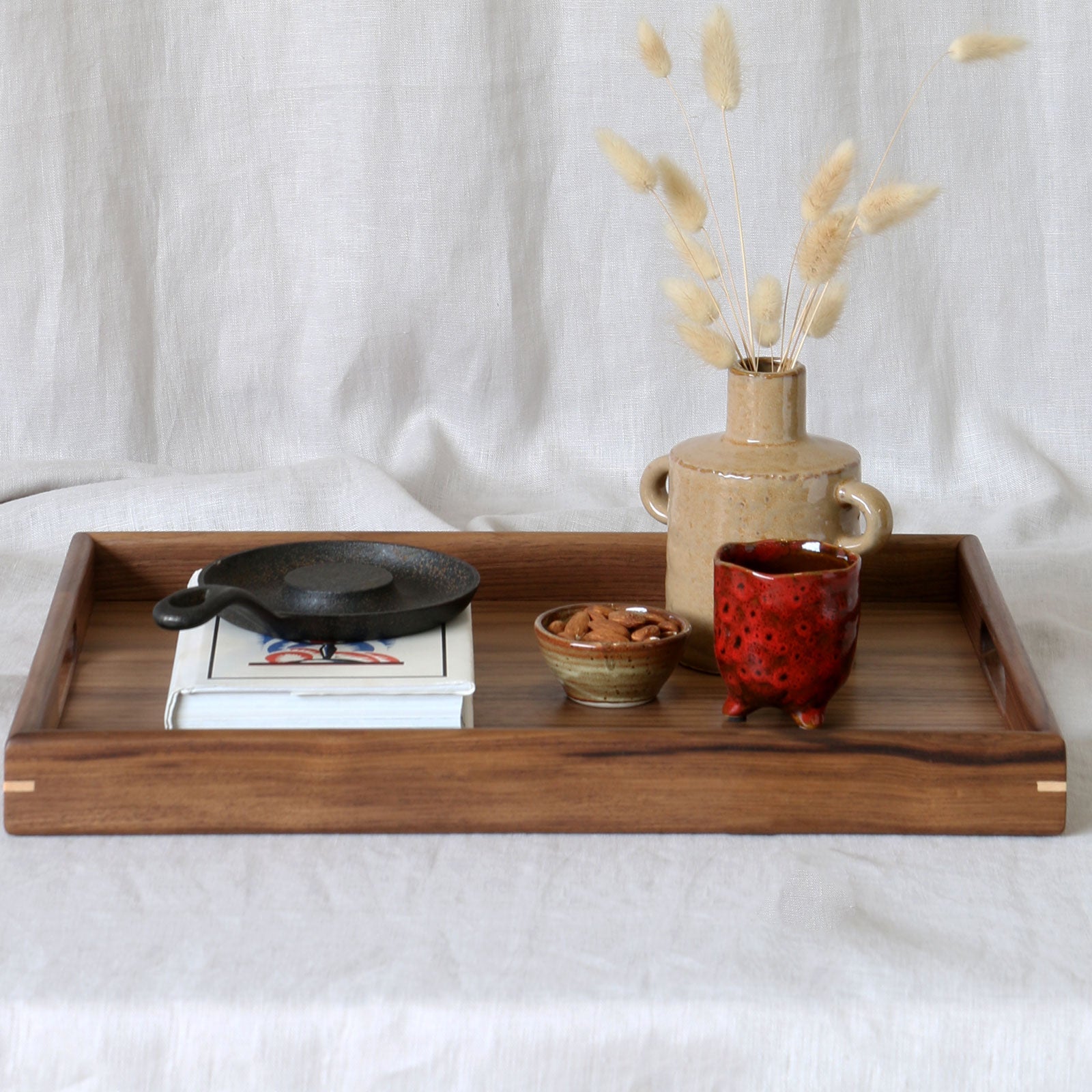A walnut wooden ottoman tray adorned with artisanal objects, perfect for elegant home decor.