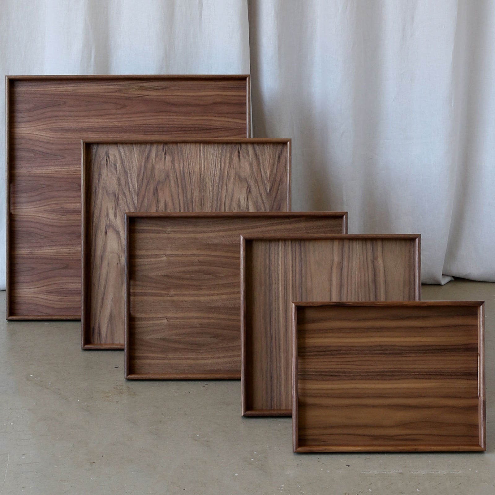 A set of five handcrafted wooden trays for footstools in rich walnut, arranged in descending sizes, showcasing their smooth finish and natural wood grain.