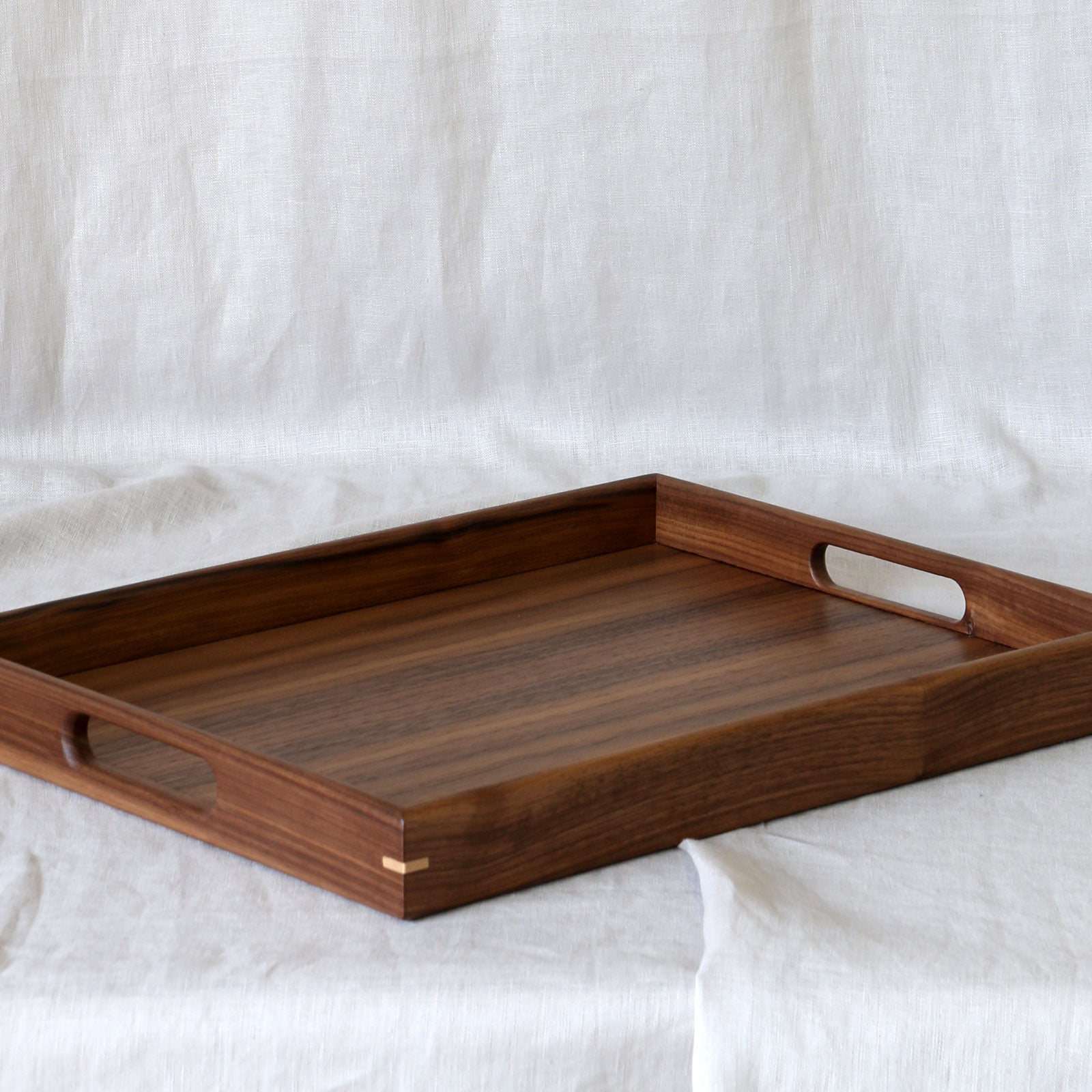 A decorative walnut serving tray with cut-out handles, set against a neutral fabric backdrop.