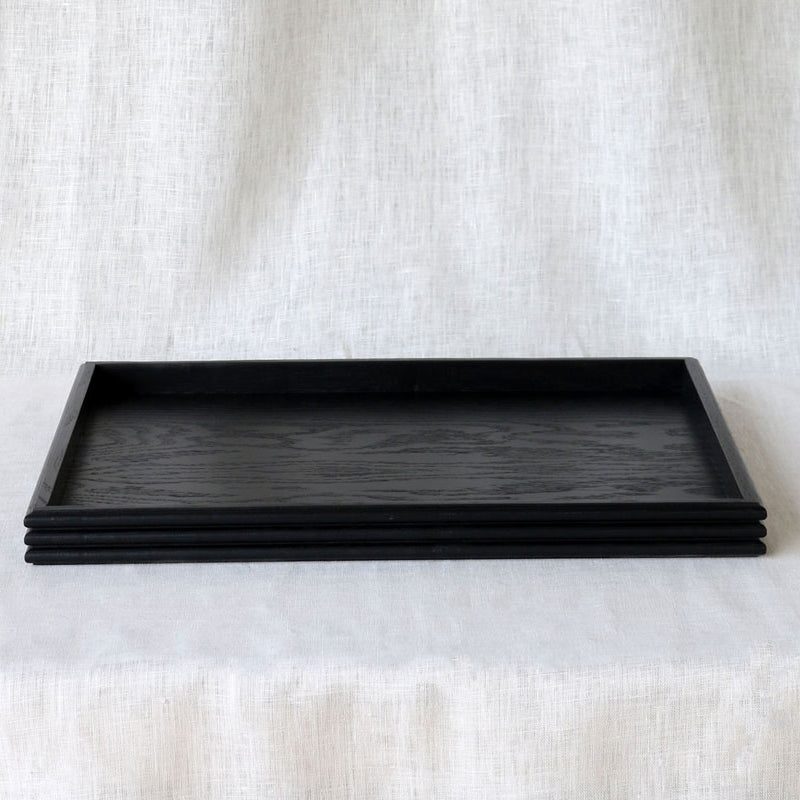 Front view of an empty rectangular black wooden tray, showcasing its minimalist design and stacked reeded edge detail.