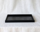 Front view of an empty rectangular black wooden tray, showcasing its minimalist design and stacked reeded edge detail.