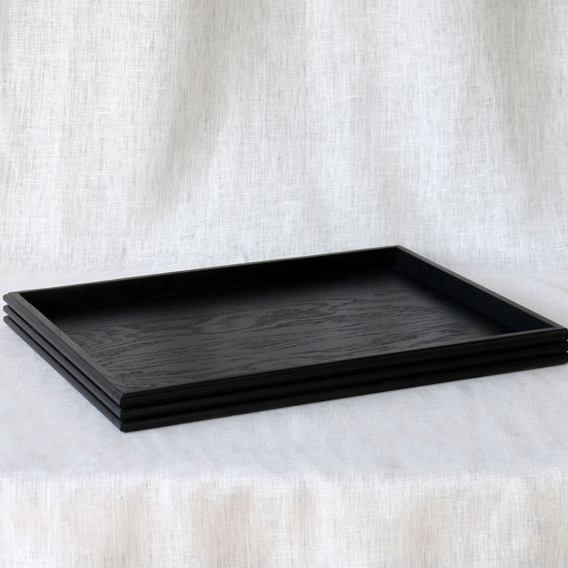 Angled side view of the black tray highlighting the clean lines, low-profile edge, and visible wood grain pattern
