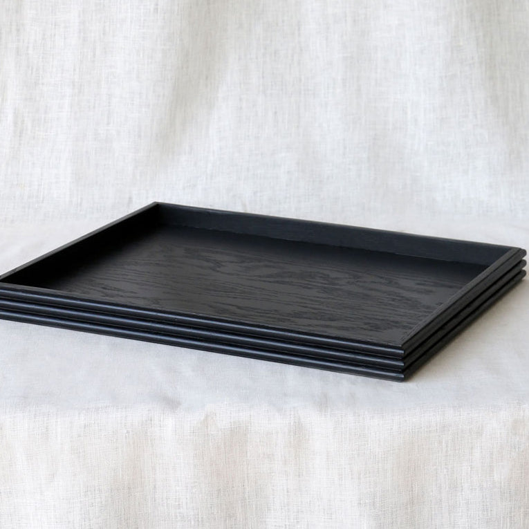 Three-quarter view of the black wooden tray resting on a linen-covered surface, emphasizing the handcrafted reeded edges and matte finish.