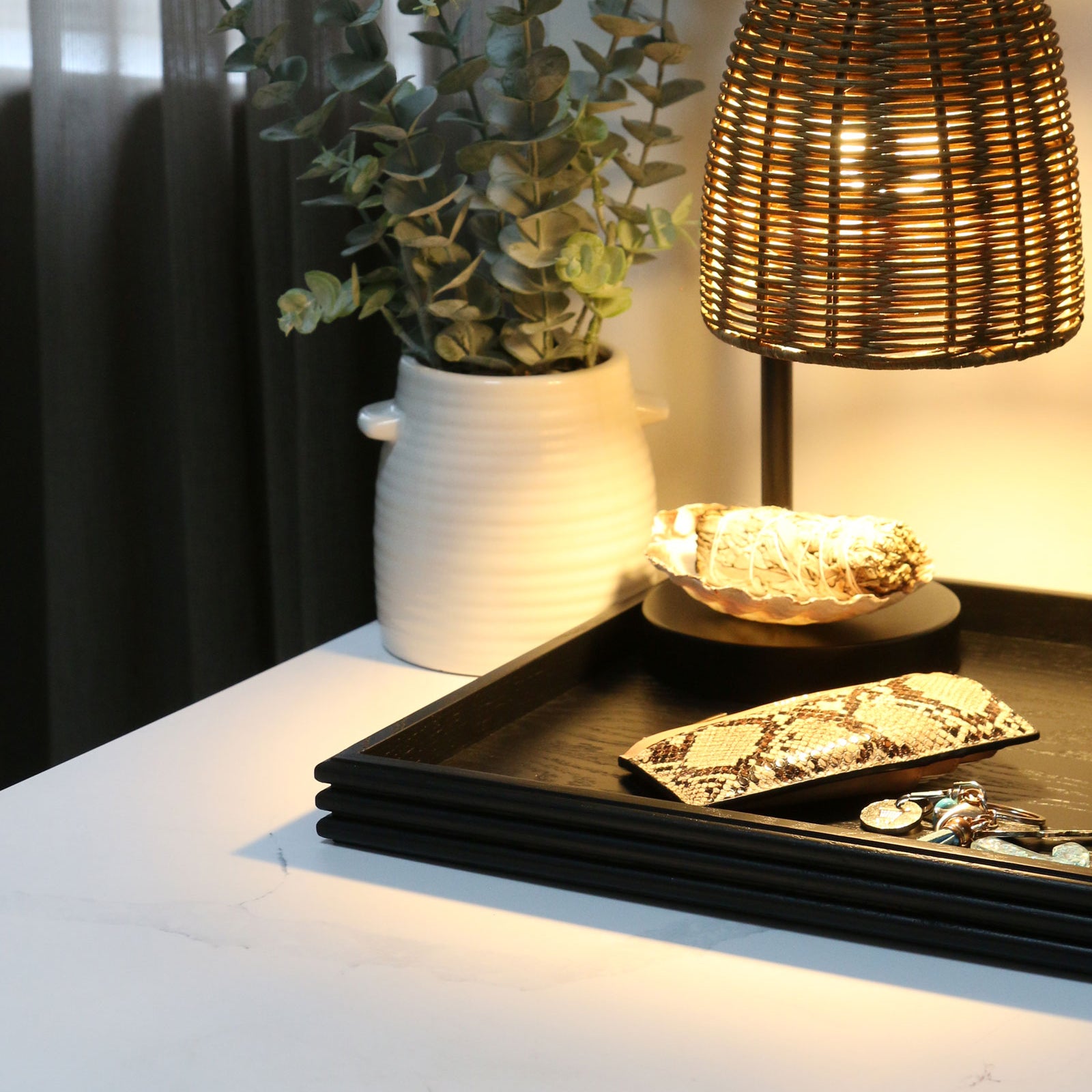 A coffee table tray in black wood, placed on a nightstand, holding keys, a wallet, and a book, serving as a stylish and functional bedside organizer.