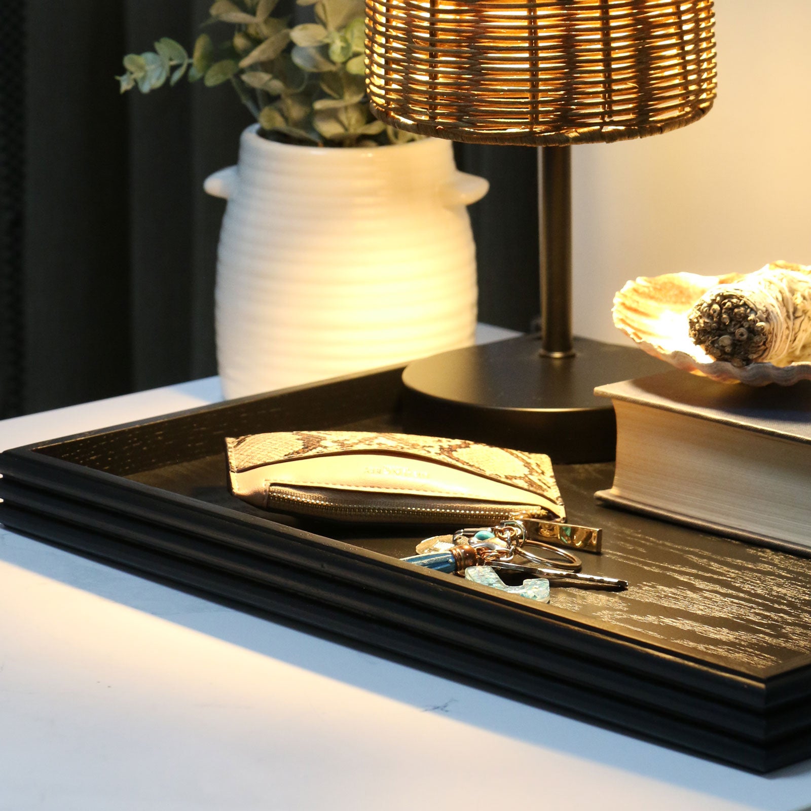 A decorative tray in black wood, styled on a modern nightstand with a woven lamp, a vase with greenery, and a sage bundle, adding warmth and sophistication to the space.
