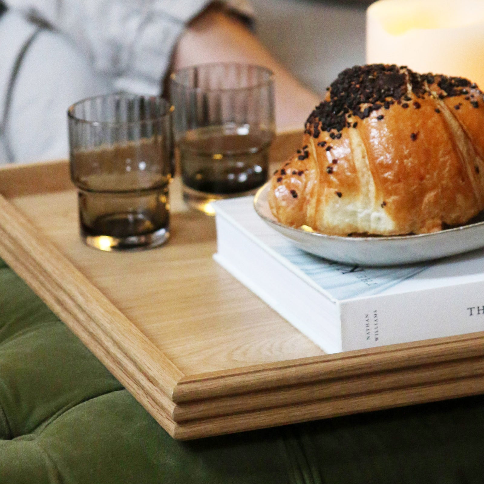 A decorative tray with a reeded wood design, styled with croissants, a book, and candles, offering a refined touch to a modern home aesthetic.