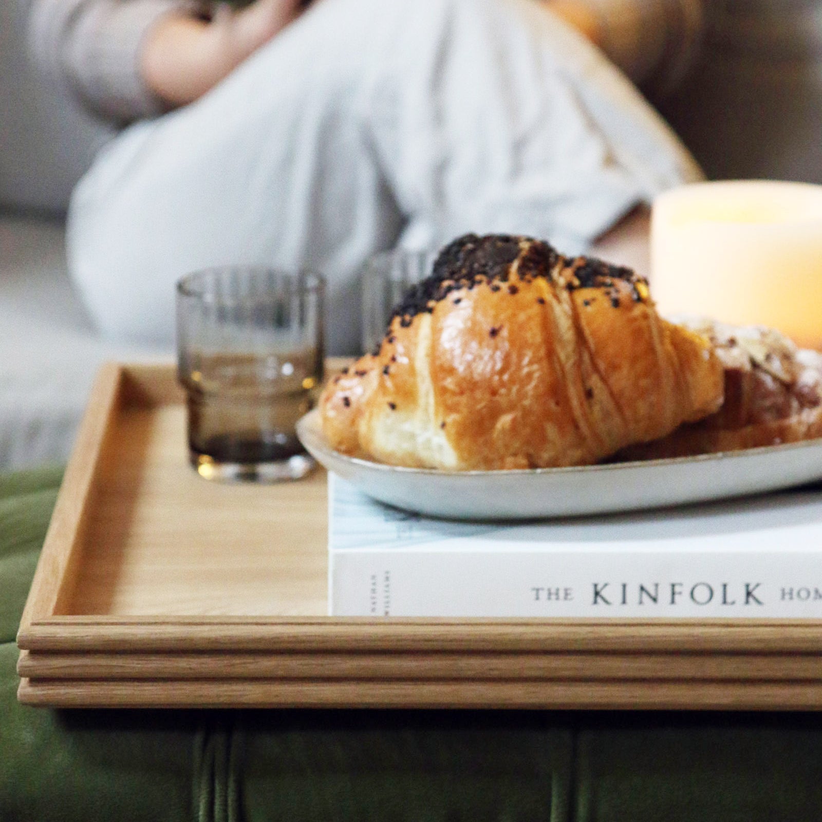A wooden tray for a footstool, featuring a handcrafted oak design with reeded edges, elegantly styled with pastries, a book, and a candle in a cozy living room setting.