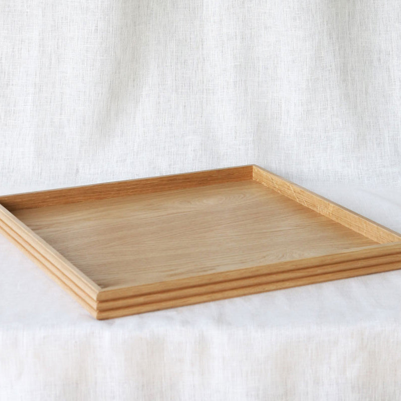 Angled shot of the empty oak tray, highlighting its minimalist design, raised edges, and reeded detail against a neutral fabric background.