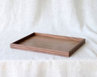 Slightly angled top-down view of the empty walnut wooden tray, emphasizing the natural wood grain and minimalist raised edge.