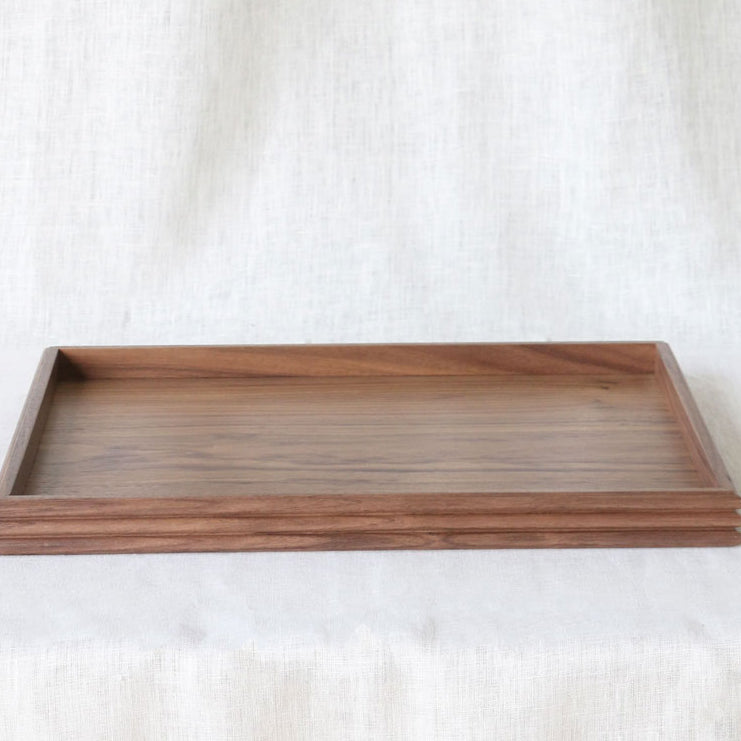 Front-facing image of the walnut tray on a table covered with light linen, displaying its compact, functional form and elegant craftsmanship.