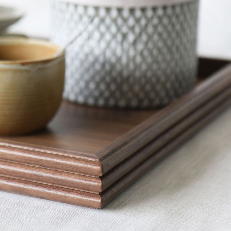 Close-up of the tray’s corner, capturing the reeded detailing, warm walnut tone, and part of the styled scene with a ceramic cup and textured plant pot.