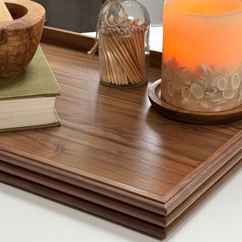 A handcrafted tray in walnut, set on a kitchen counter, styled with a candle, books, and a mortar and pestle, adding a sophisticated touch to the decor.