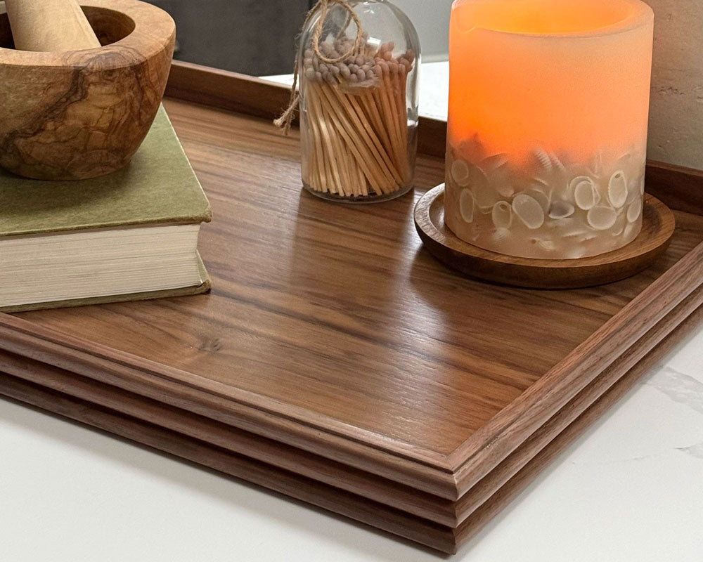 A handcrafted tray in walnut, set on a kitchen counter, styled with a candle, books, and a mortar and pestle, adding a sophisticated touch to the decor.