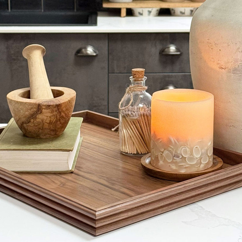 A coffee table tray in dark walnut, featuring elegant reeded edges, styled with books and a candle in a contemporary kitchen setting.