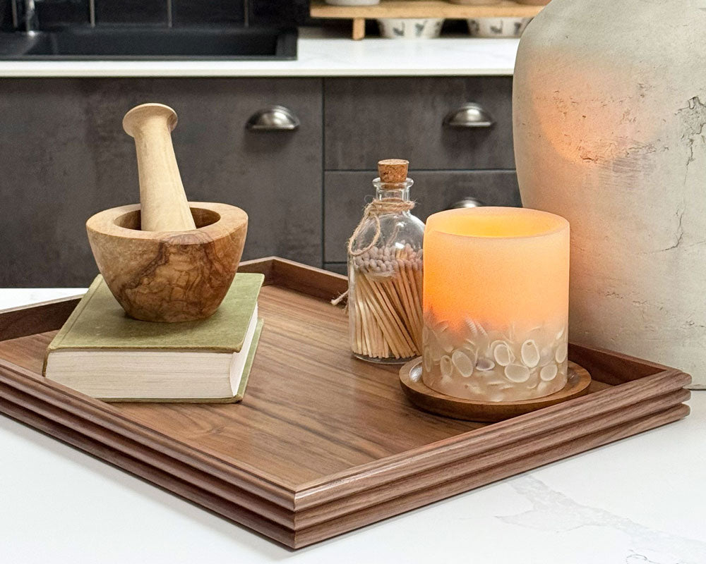 A coffee table tray in dark walnut, featuring elegant reeded edges, styled with books and a candle in a contemporary kitchen setting.