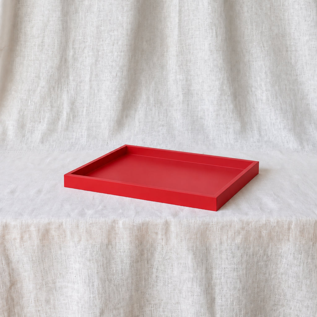 A bright cherry-red rectangular tray with raised edges, placed on a draped off-white fabric surface against a matching fabric backdrop.