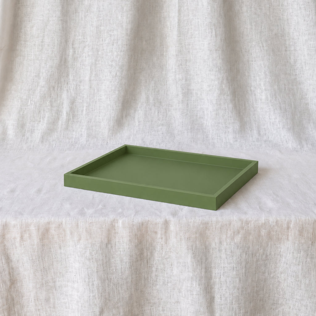 A rectangular olive green tray with raised edges, displayed on a white textured fabric surface against a matching draped fabric backdrop.