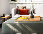 Large wooden ottoman tray placed on a green footstool in a cozy living room, featuring a yellow book and a sculptural black vase.