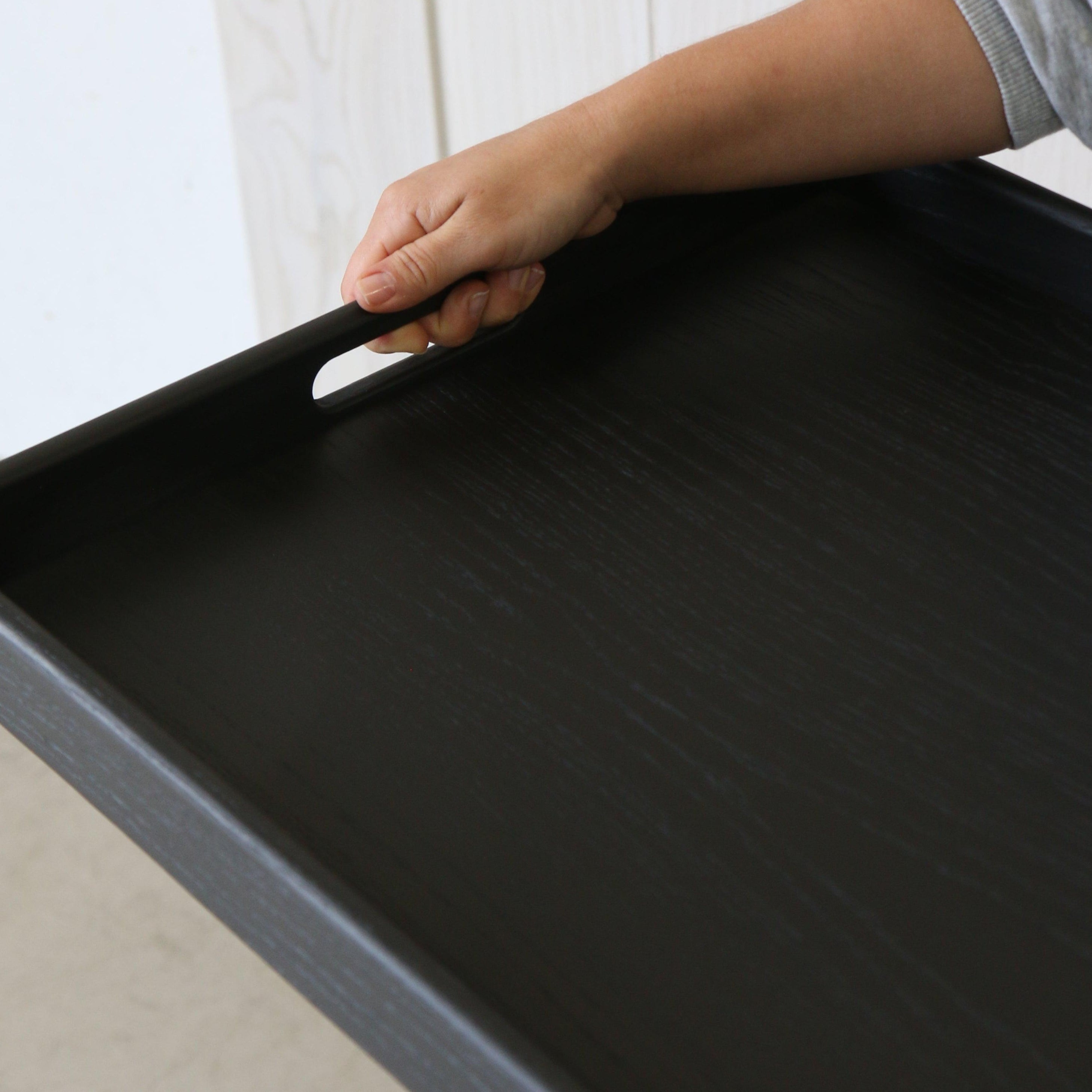Close-up of a handcrafted tray in black being held by a person, highlighting the smooth wooden texture and built-in handle.