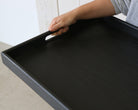 Close-up of a handcrafted tray in black being held by a person, highlighting the smooth wooden texture and built-in handle.