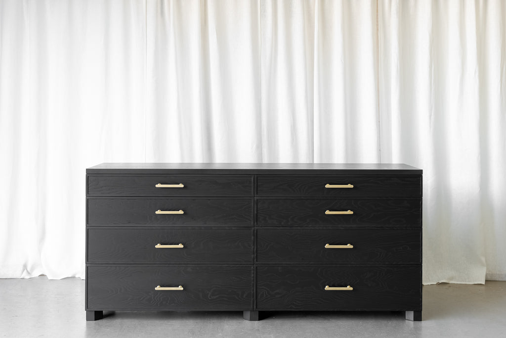Black wooden sideboard, with visible wood grain. 8 drawers, antique brass handles and geometrical feet