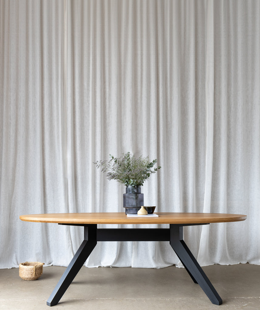 Image capturing the elegance of a styled 2.2-meter oval dining table, boasting a solid oak tabletop atop a sleek black base, timeless design and sophistication.