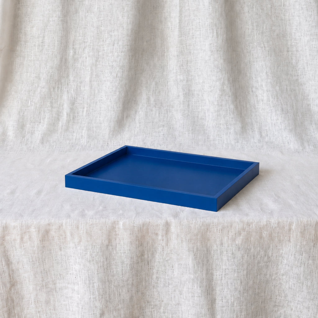 A rectangular blue tray with raised edges, placed on a draped off-white fabric surface against a matching fabric backdrop.