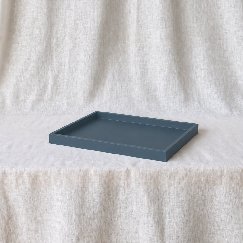 A rectangular matte slate blue tray resting on a draped off-white linen fabric background.