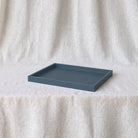 A rectangular matte slate blue tray resting on a draped off-white linen fabric background.