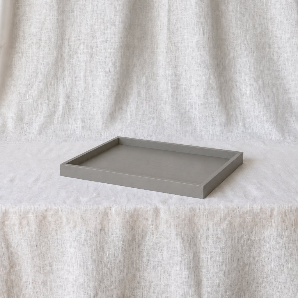 A rectangular gray concrete tray with a matte finish, displayed on a white textured fabric surface against a matching draped fabric backdrop.