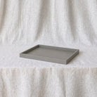 A rectangular gray concrete tray with a matte finish, displayed on a white textured fabric surface against a matching draped fabric backdrop.