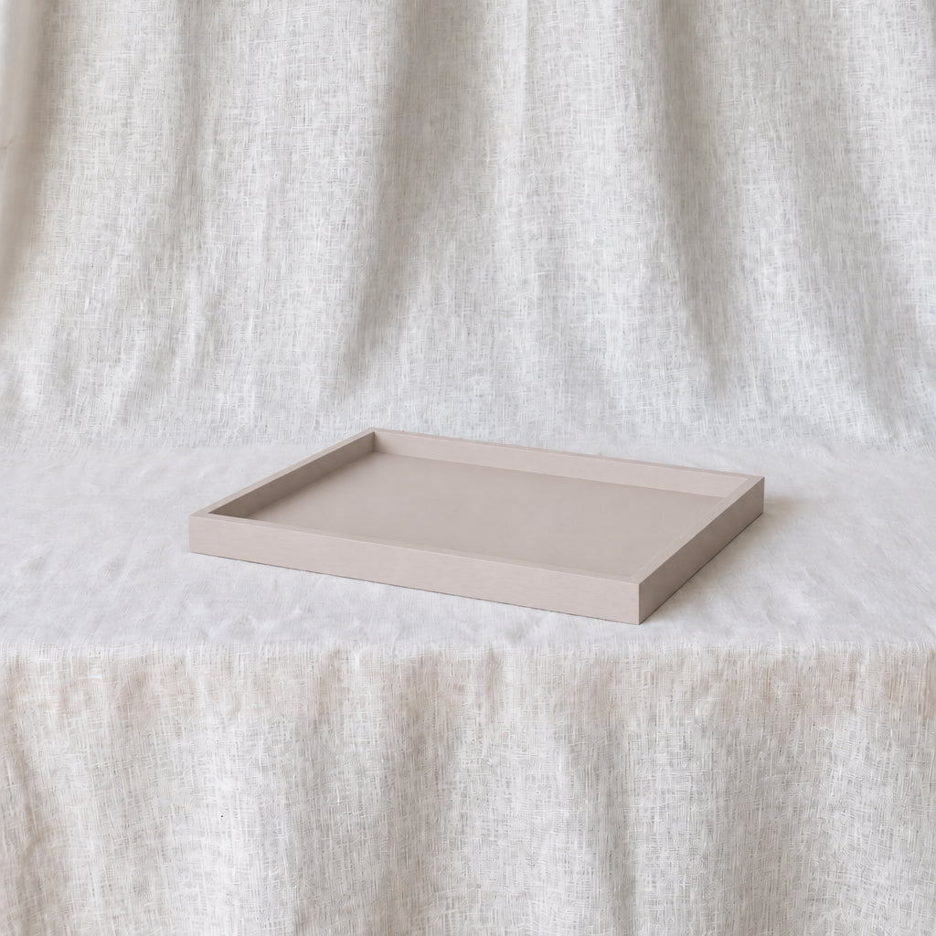 A rectangular shallow tray in a light warm dusty pink, photographed on a draped white fabric surface with matching fabric hanging in the background.