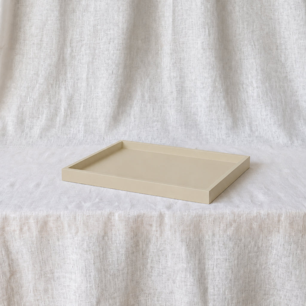 A minimalist rectangular tray with raised edges in a light beige tone, displayed on a draped white fabric surface.