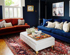 A wooden tray for footstool in a vibrant living room setting, styled with books, a candle, and flowers.