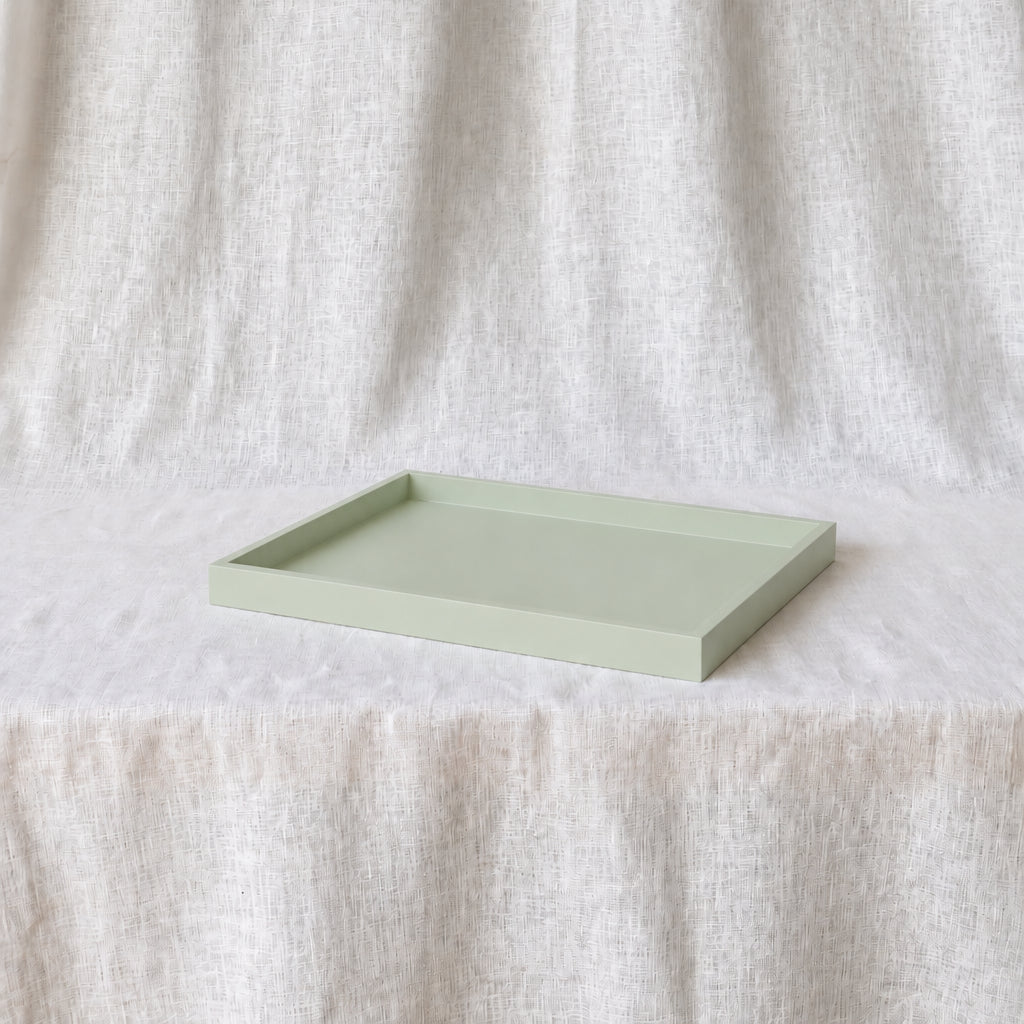 A rectangular light aquamarine tray with a raised rim, resting on a white textured fabric surface against a matching draped fabric backdrop.