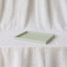 A rectangular light aquamarine tray with a raised rim, resting on a white textured fabric surface against a matching draped fabric backdrop.