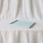 A rectangular light blue tray with raised edges, resting on a draped cream linen fabric backdrop.