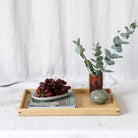 Wooden tray with grapes, a vase of eucalyptus, and a book on a white background