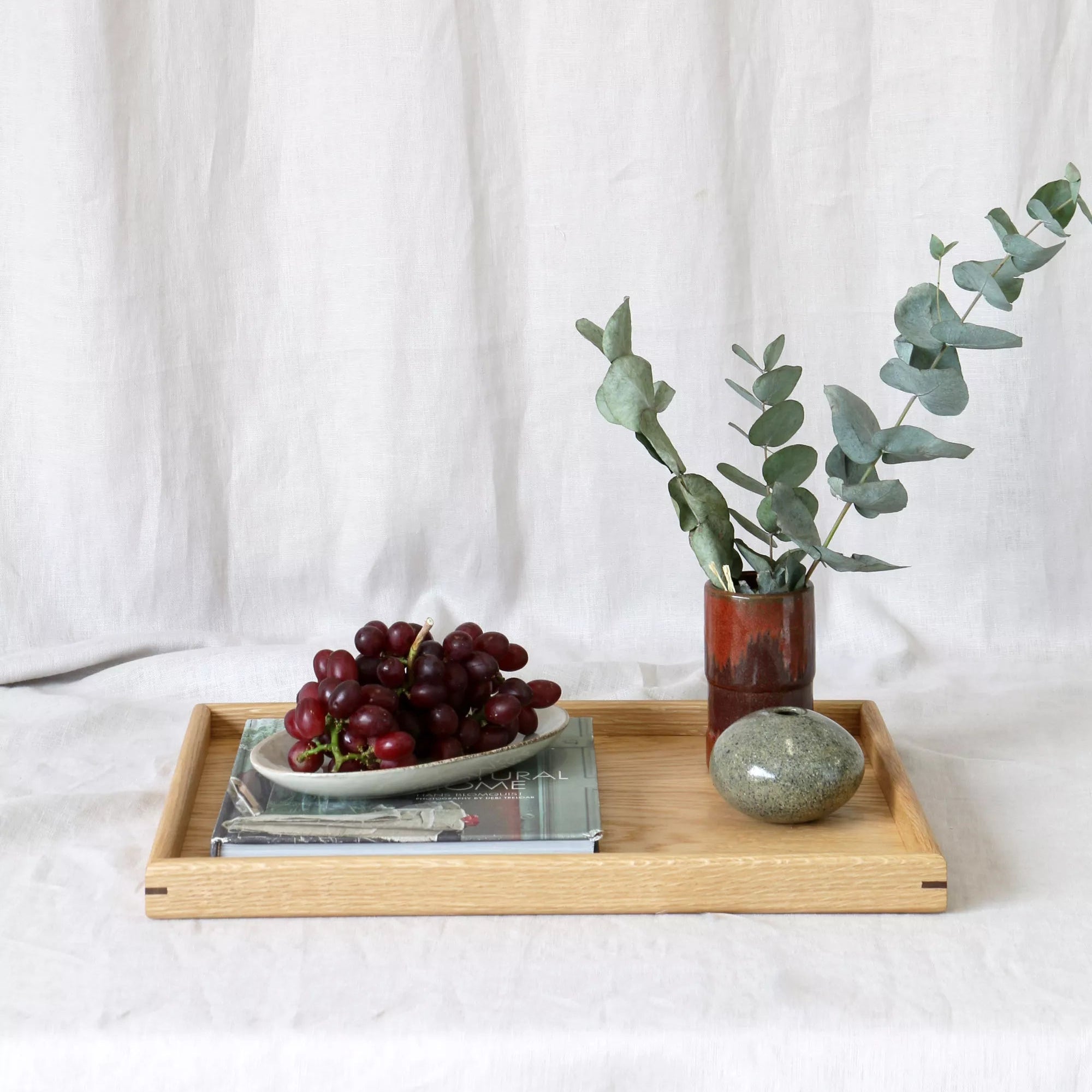 Wooden tray with grapes, a vase of eucalyptus, and a book on a white background