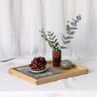 Wooden oak tray with grapes, a vase of eucalyptus on a white fabric background. A large coffee table tray, featuring fine joinery details and a natural oak finish, is designed for functional elegance.