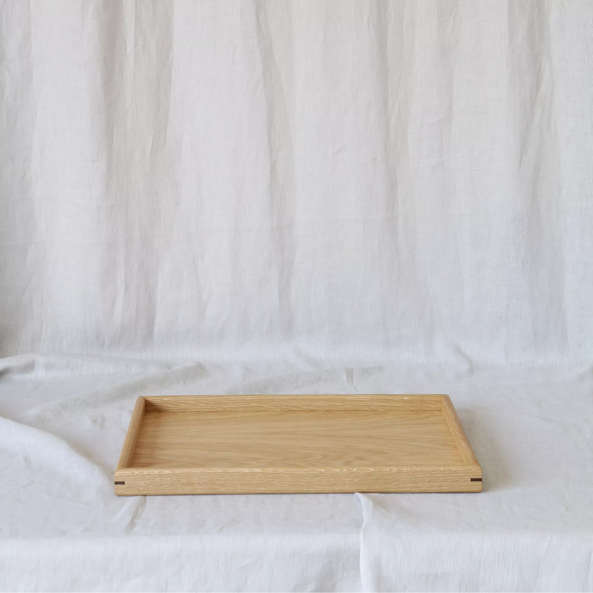 A medium-sized wooden tray for footstool, crafted from oak, displayed on a neutral fabric background.