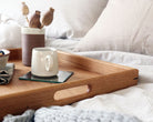 Side view of a large decorative tray with handles, elegantly styled on a bed with neutral linens and cozy textures.