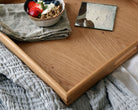 Close-up of a handcrafted wooden tray, showcasing a bowl of yogurt with granola and fresh berries, set on a soft gray blanket.