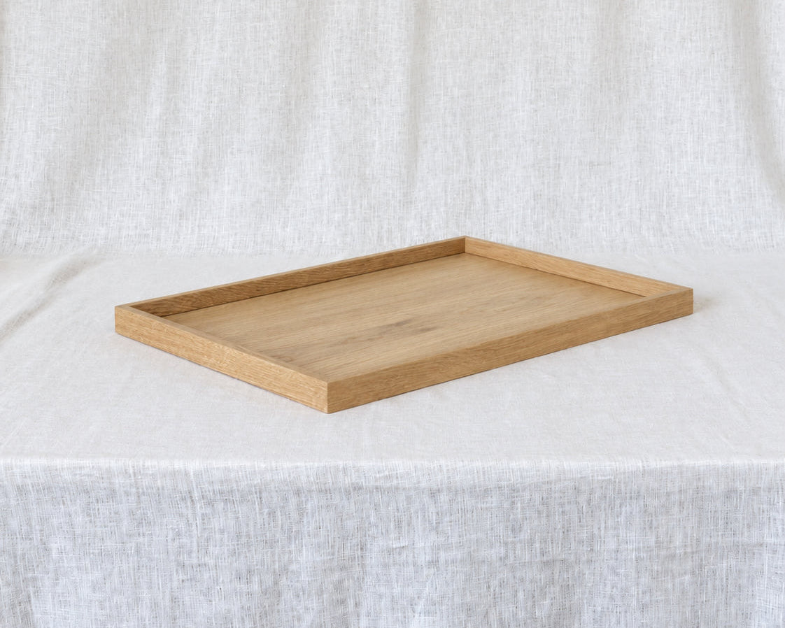 A rectangular wooden serving tray with a light oak finish, set on a draped white linen fabric background.