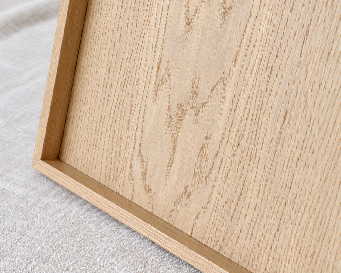 Close-up of a light natural oak wood serving tray resting on a textured light beige linen fabric background.